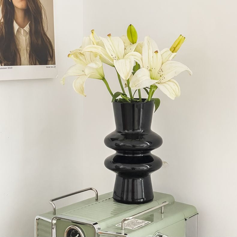 Black sculptural glass vase holding white lilies on stacked books