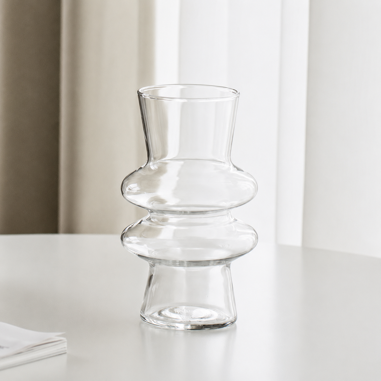 Clear modern sculptural glass flower vase on a white table