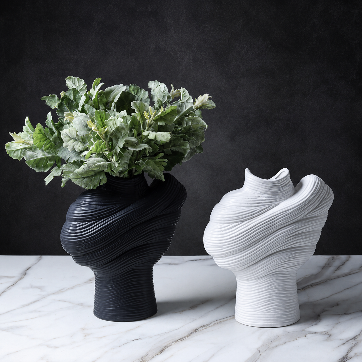 Black ribbed ceramic vase with foliage beside a white sculptural vase