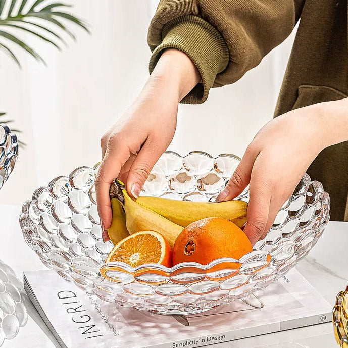 Clear textured glass bowl with hands arranging oranges and fruit inside