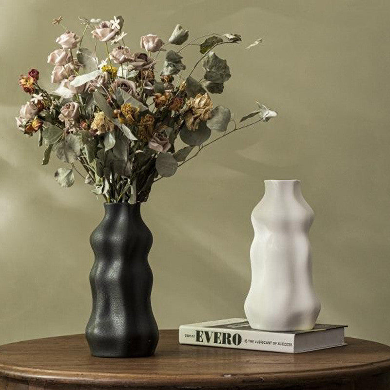 Black and white modern wavy ceramic vases displayed with dried flowers on a wooden table