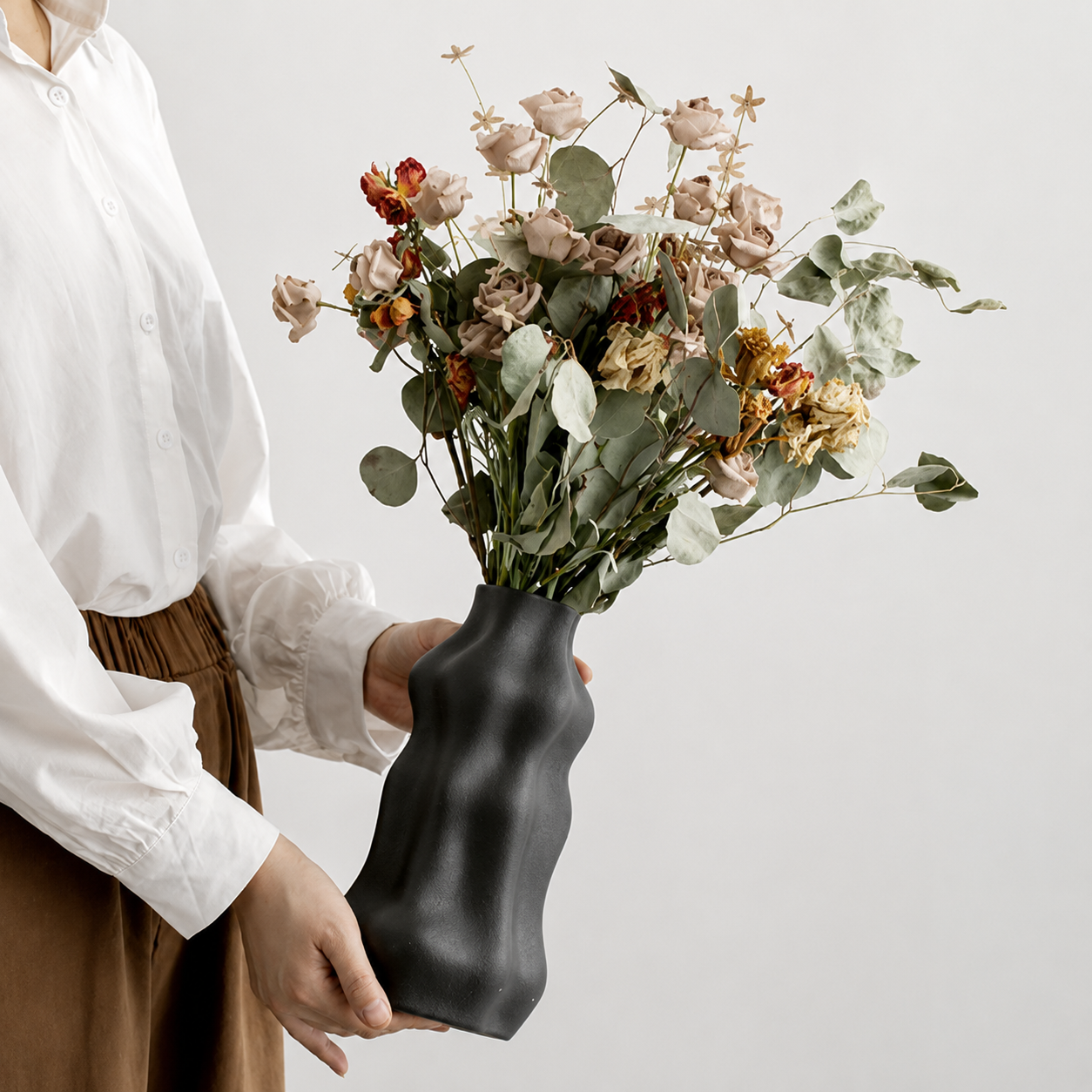 Person holding a black wavy ceramic vase filled with dried flowers