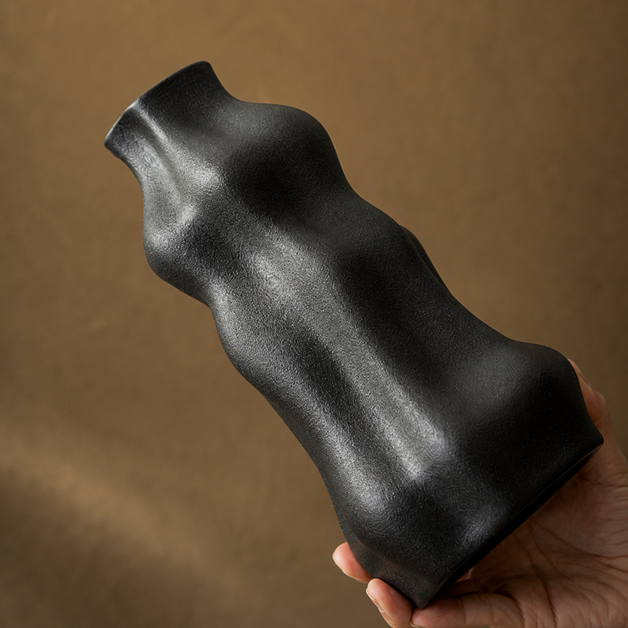 Close up of a black sculptural ceramic vase held horizontally