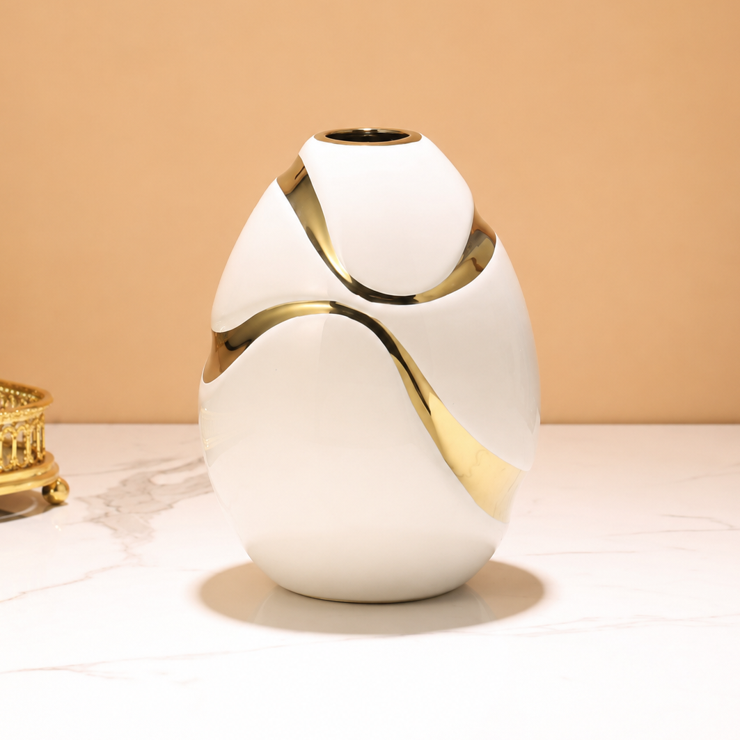 Rounded white ceramic vase with flowing gold accents against a warm beige background