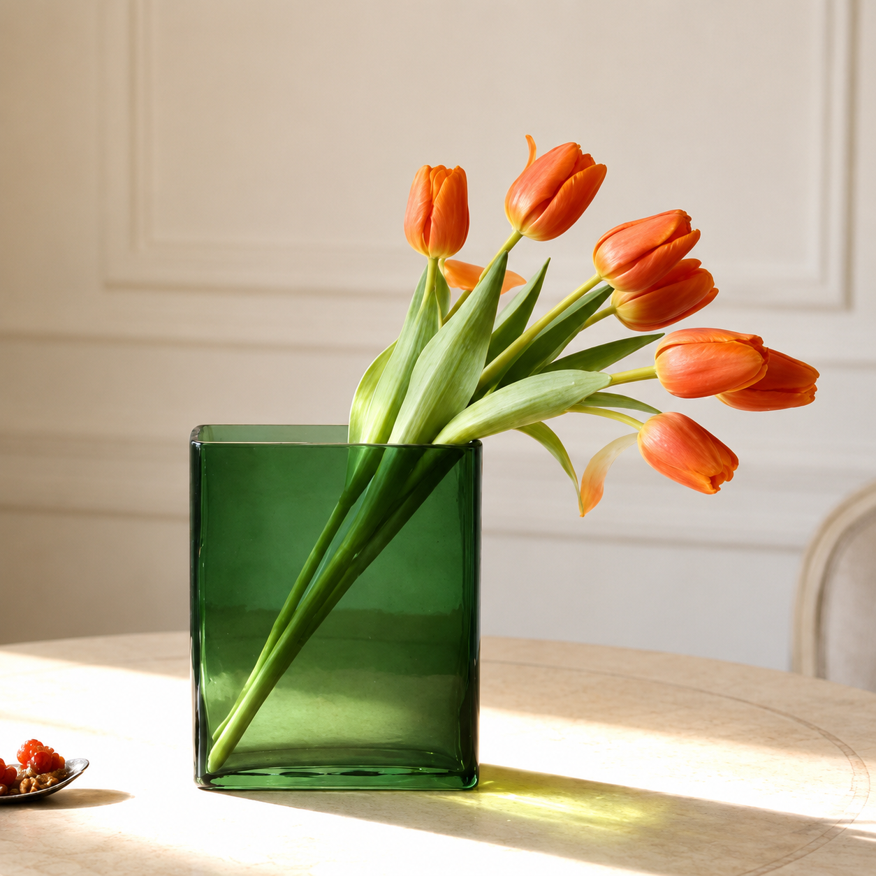 Green rectangular hand blown glass vase with orange tulips on a sunlit table