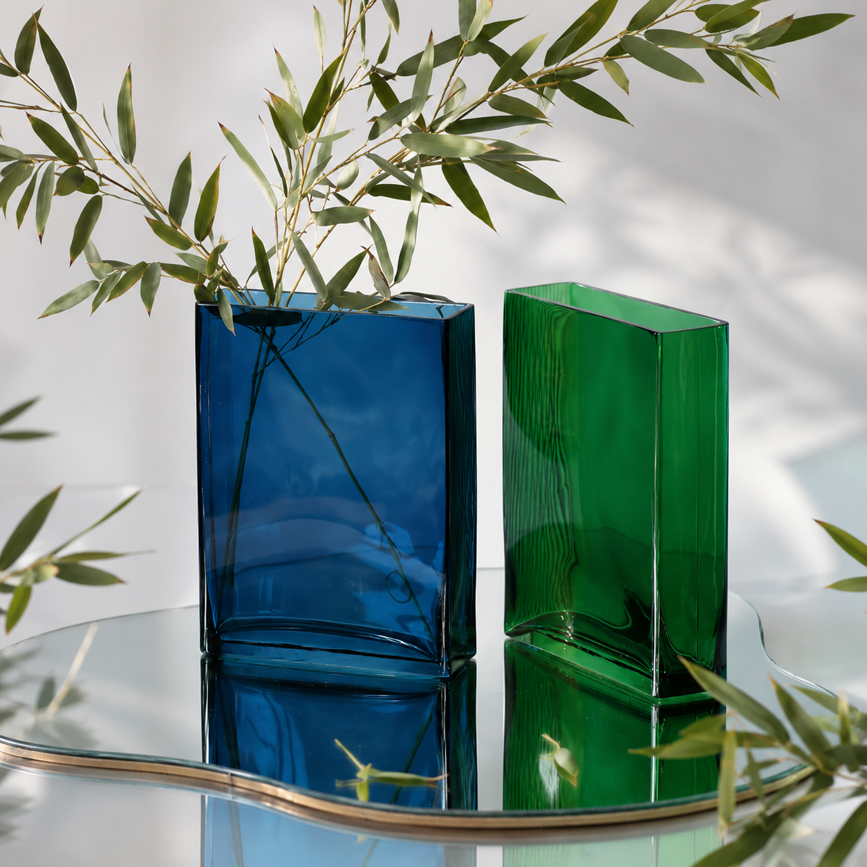 Blue and green rectangular glass vases with olive branches on a mirrored surface