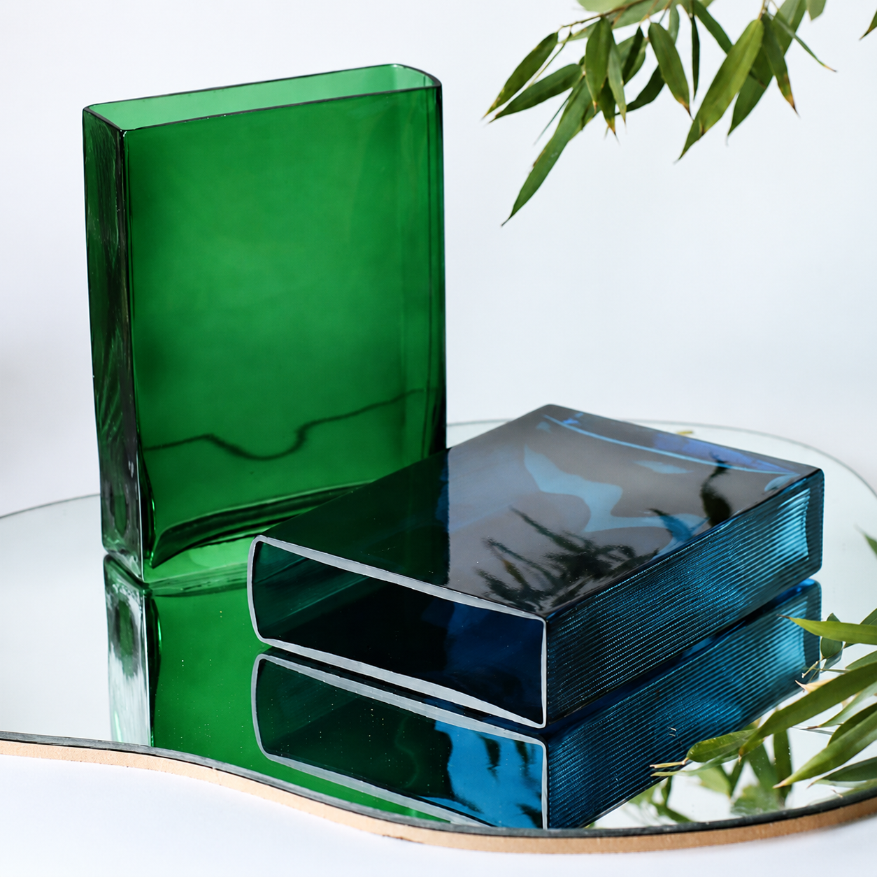 Blue and green hand blown glass vases displayed horizontally and upright on a reflective surface