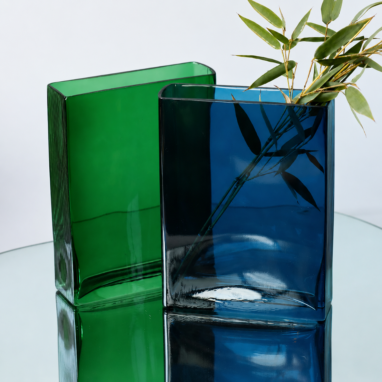 Blue and green rectangular glass vases styled with olive branches on a mirrored tray