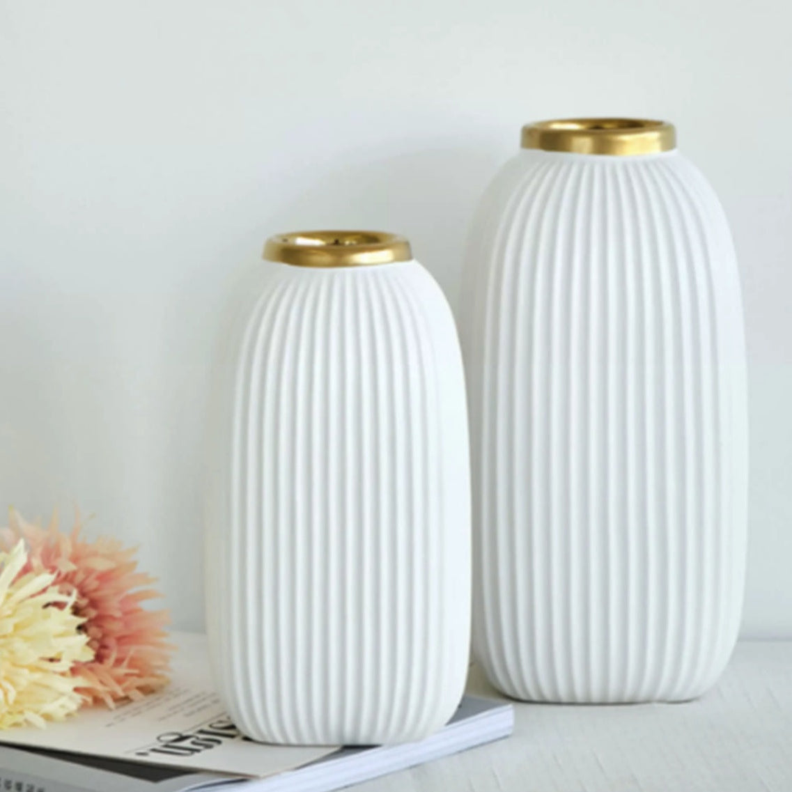 Ribbed white ceramic vases with gold rims styled on a book with soft flowers