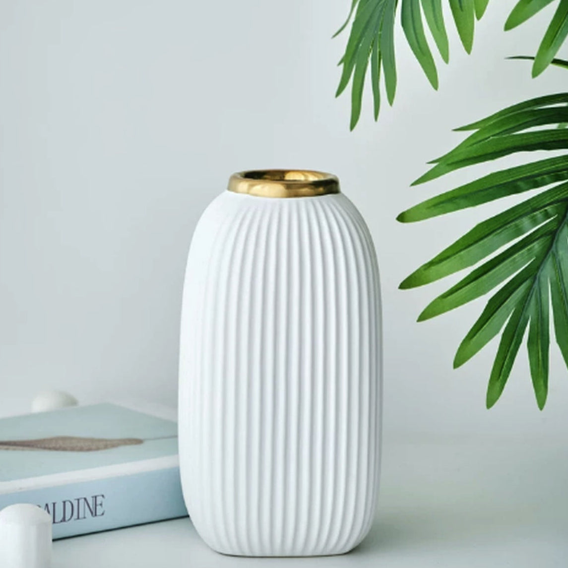 Large ribbed white ceramic vase with gold rim styled with green palm leaves