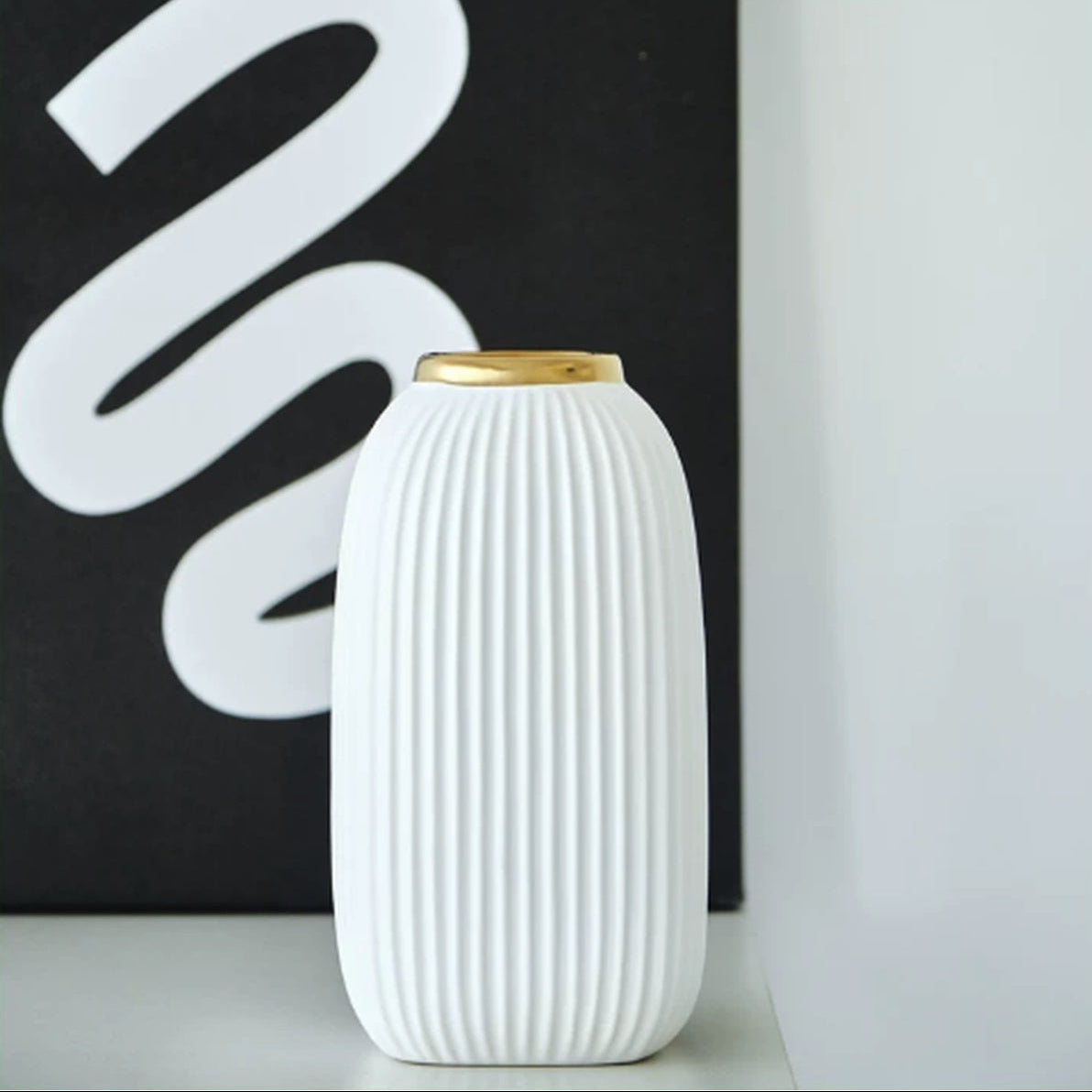 Modern white ribbed ceramic vase with gold rim displayed beside black wall art