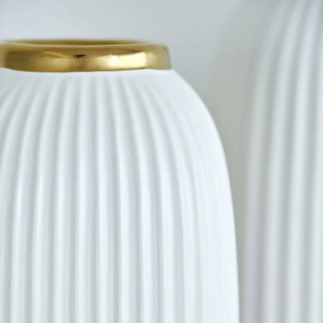 Close up of vertical ribbed texture on white ceramic vase with gold rim