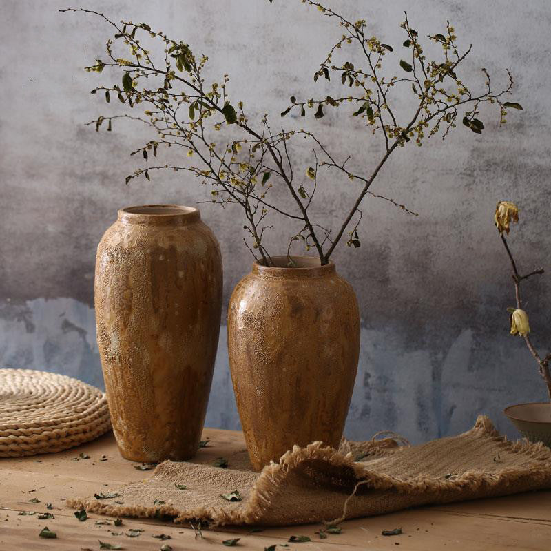 Two tall rustic brown textured ceramic vases styled with branches on a wooden table