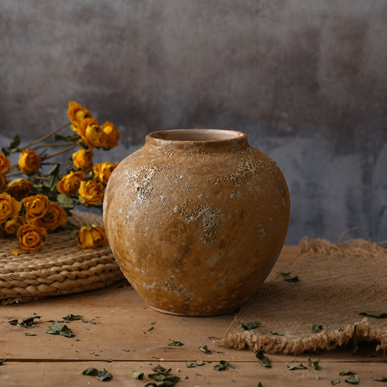 Round rustic brown textured ceramic vase on a wooden table with dried flowers