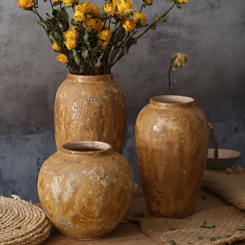 Three brown textured ceramic vases styled with yellow flowers on a wooden surface