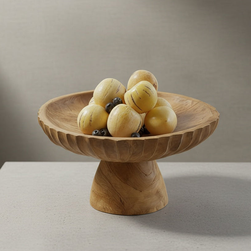 Rustic carved wood pedestal bowl filled with pale melons on a neutral tabletop