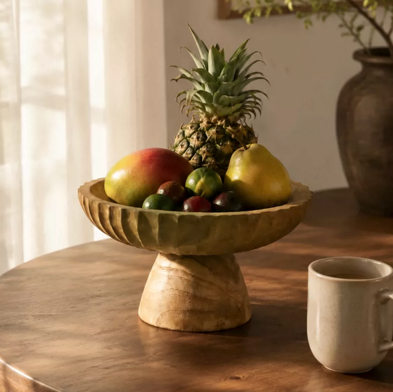 Carved wood fruit pedestal bowl styled with mixed fruit on a wooden table
