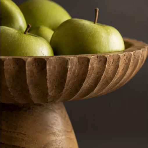 Close up of carved wood pedestal bowl filled with green apples