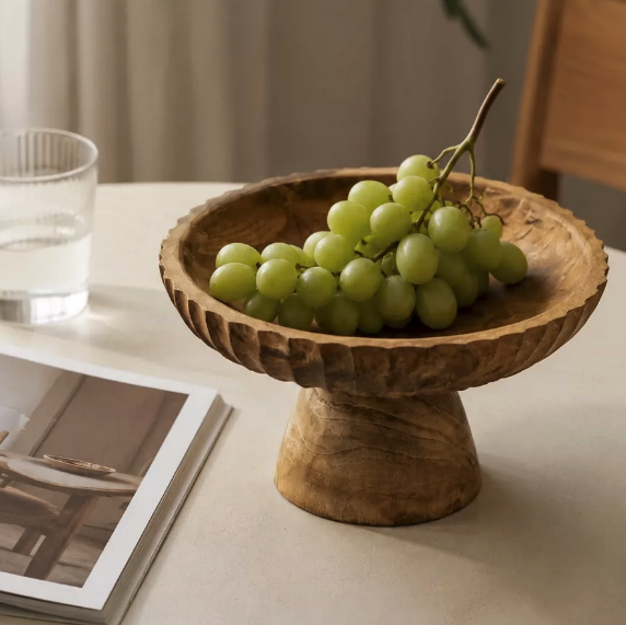 Carved wood centerpiece bowl with green grapes on a table with soft neutral styling