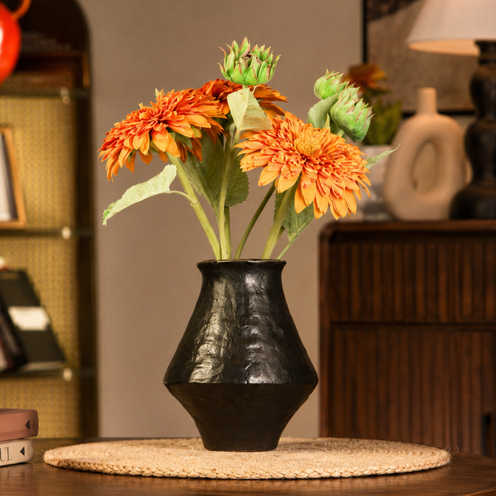 Black rustic ceramic flower vase with orange flowers on a round woven placemat
