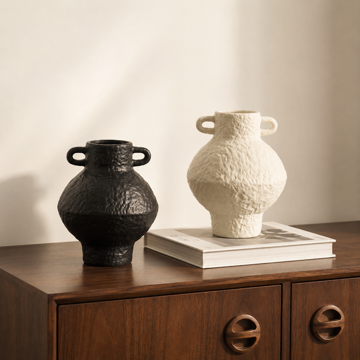 Black and ivory textured ceramic vases displayed on a wooden cabinet with a book
