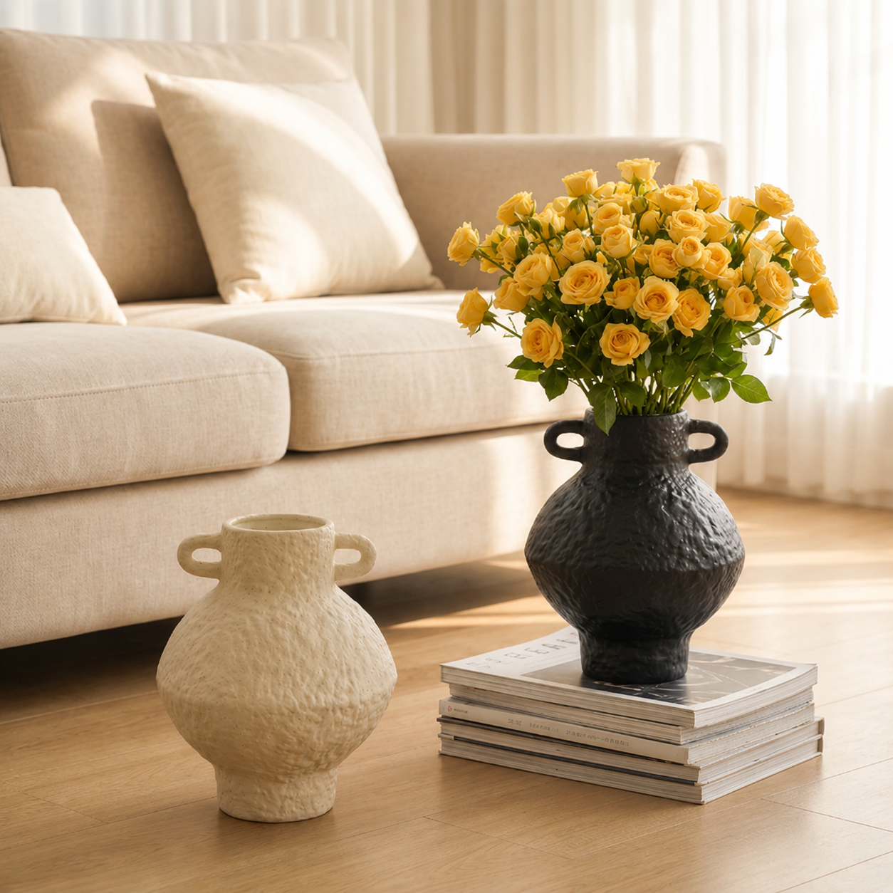 Black textured ceramic vase with yellow roses on stacked books beside an ivory handled vase in a warm living room