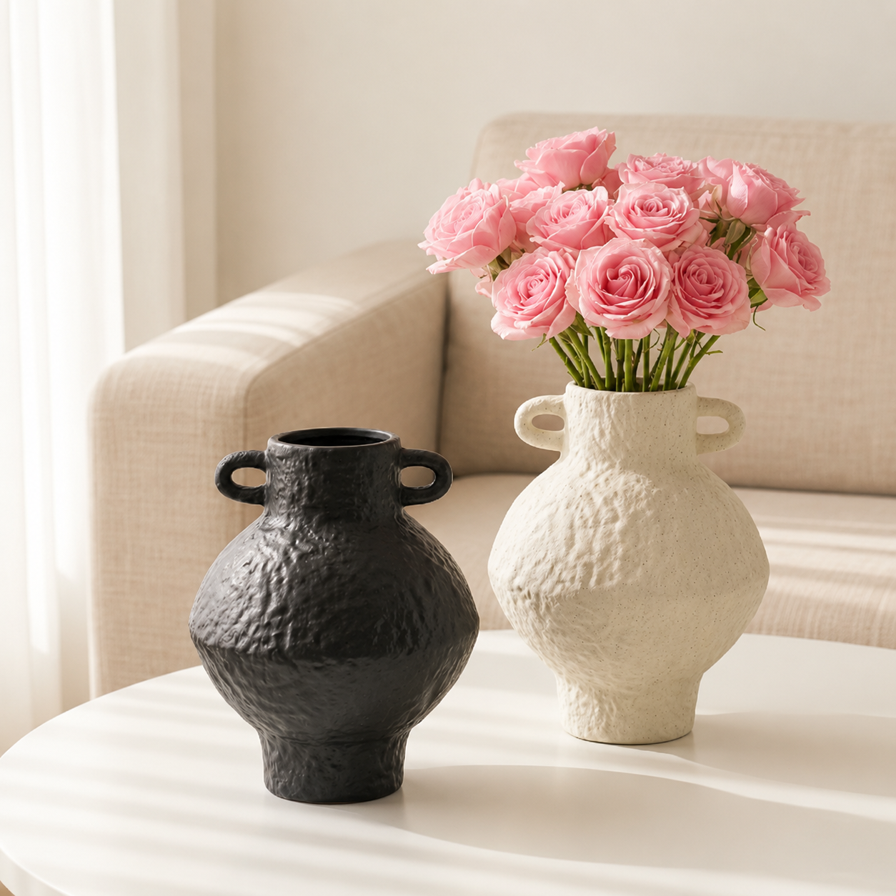 Black textured ceramic vase beside an ivory handled vase filled with pink roses on a white table
