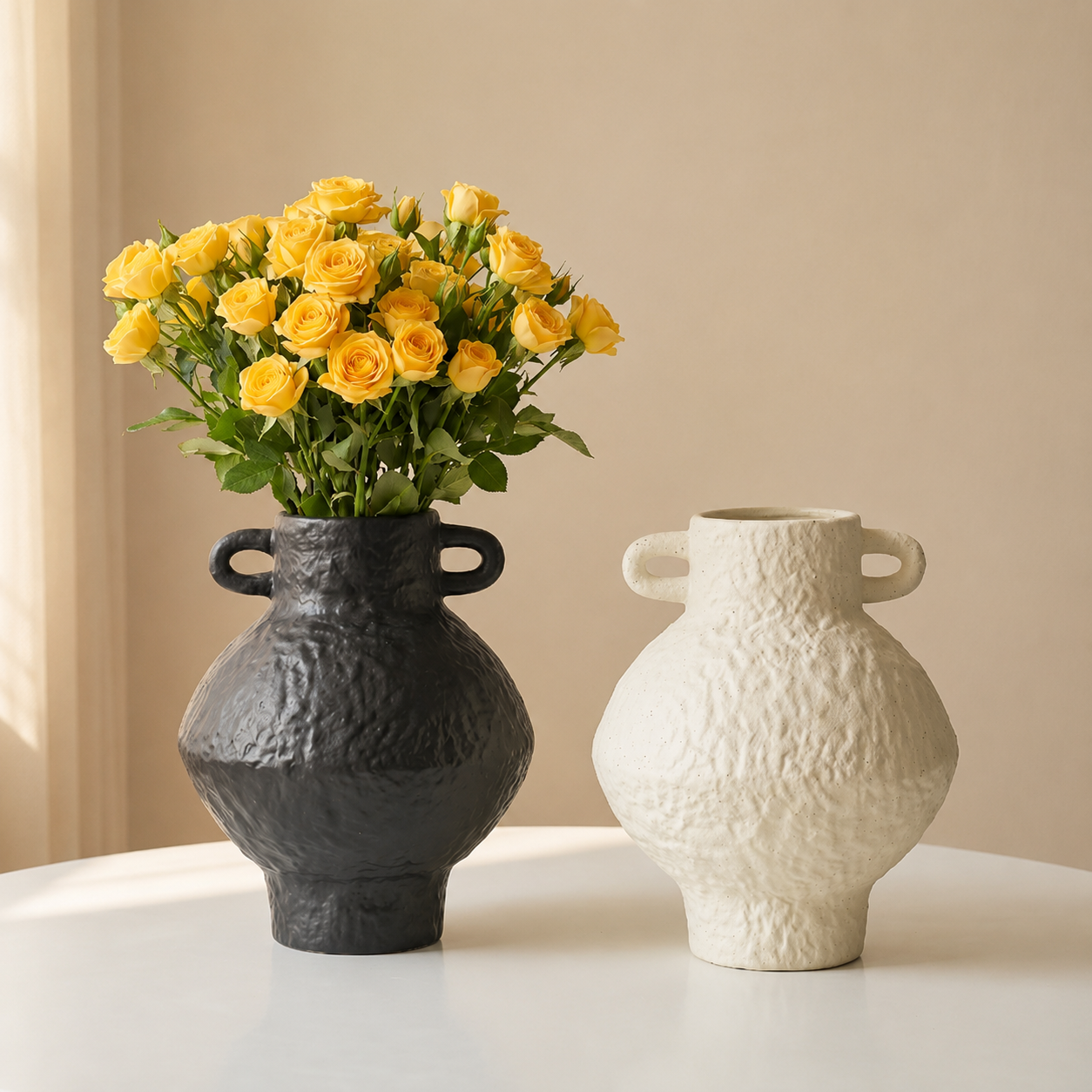 Black and ivory textured ceramic vases styled together on a white table with yellow flowers in the black vase