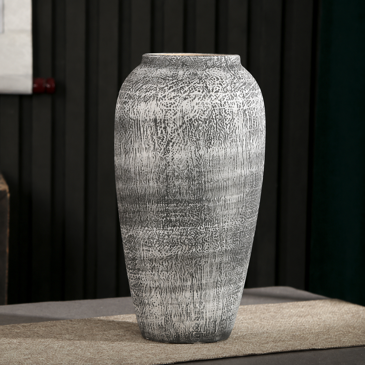 Large tall textured gray ceramic decorative vase on a neutral table runner