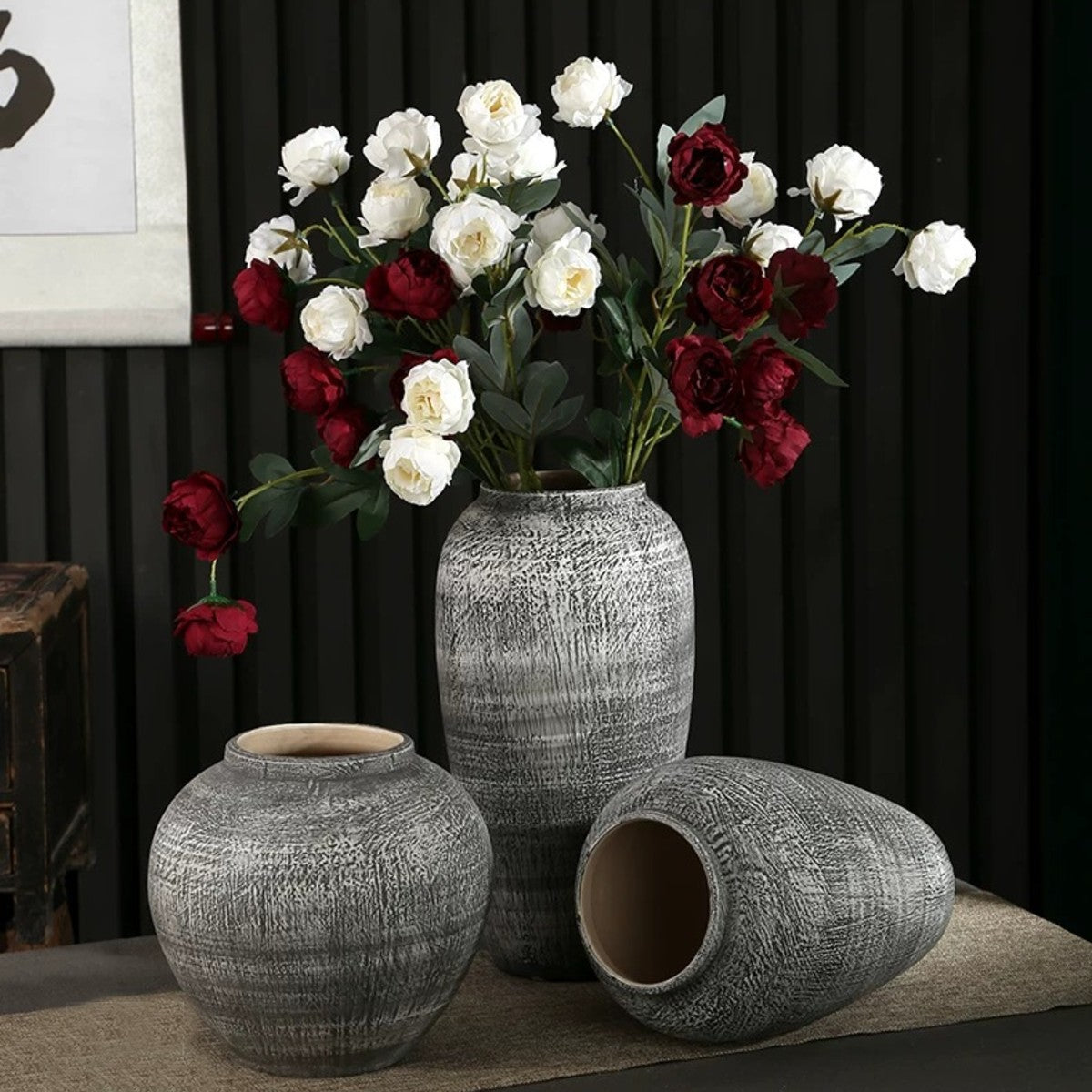 Rustic textured gray ceramic vases styled with burgundy and white flowers in a dark interior