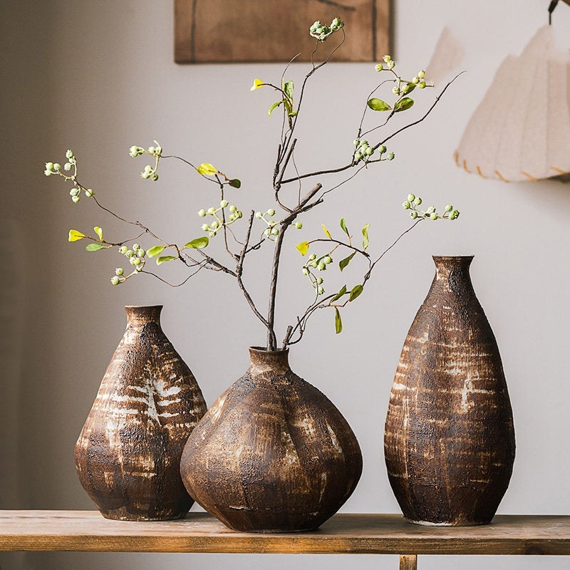 Short medium and tall rustic wabi sabi brown ceramic vases styled with leafy branches on a wooden table