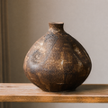 Short round rustic brown textured ceramic decorative vase on a wooden shelf
