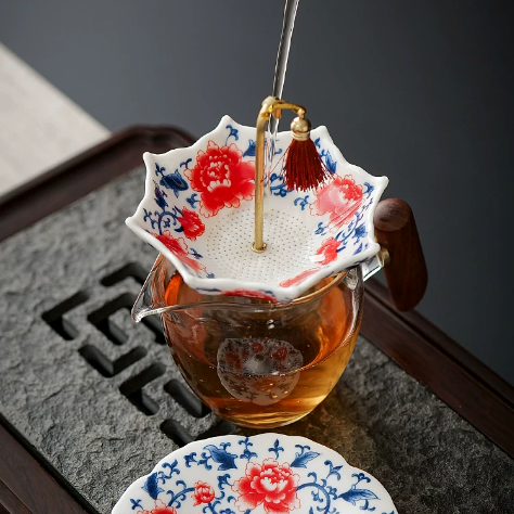 Red floral ceramic tea strainer resting over a glass pitcher of amber tea