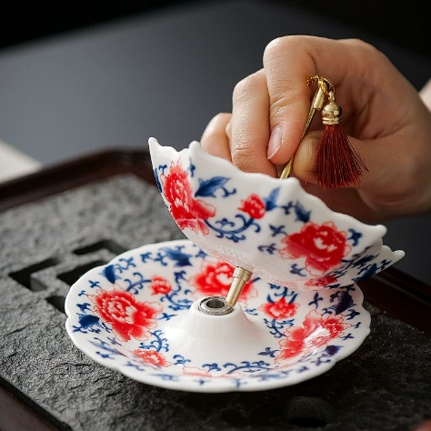 Hand lifting the red floral ceramic tea strainer above its matching drip tray