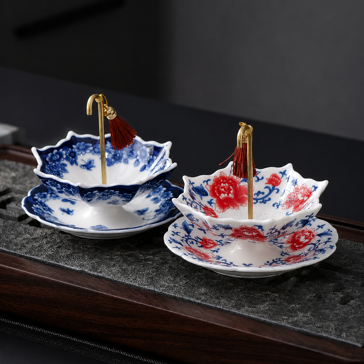 Blue floral and red floral ceramic tea strainers displayed side by side on a dark tea tray