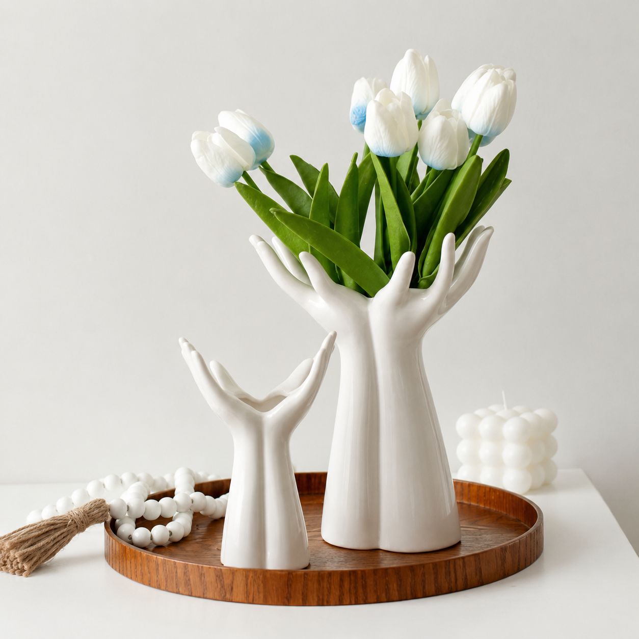 Large and medium white ceramic hand vases styled with white tulips on a wooden tray