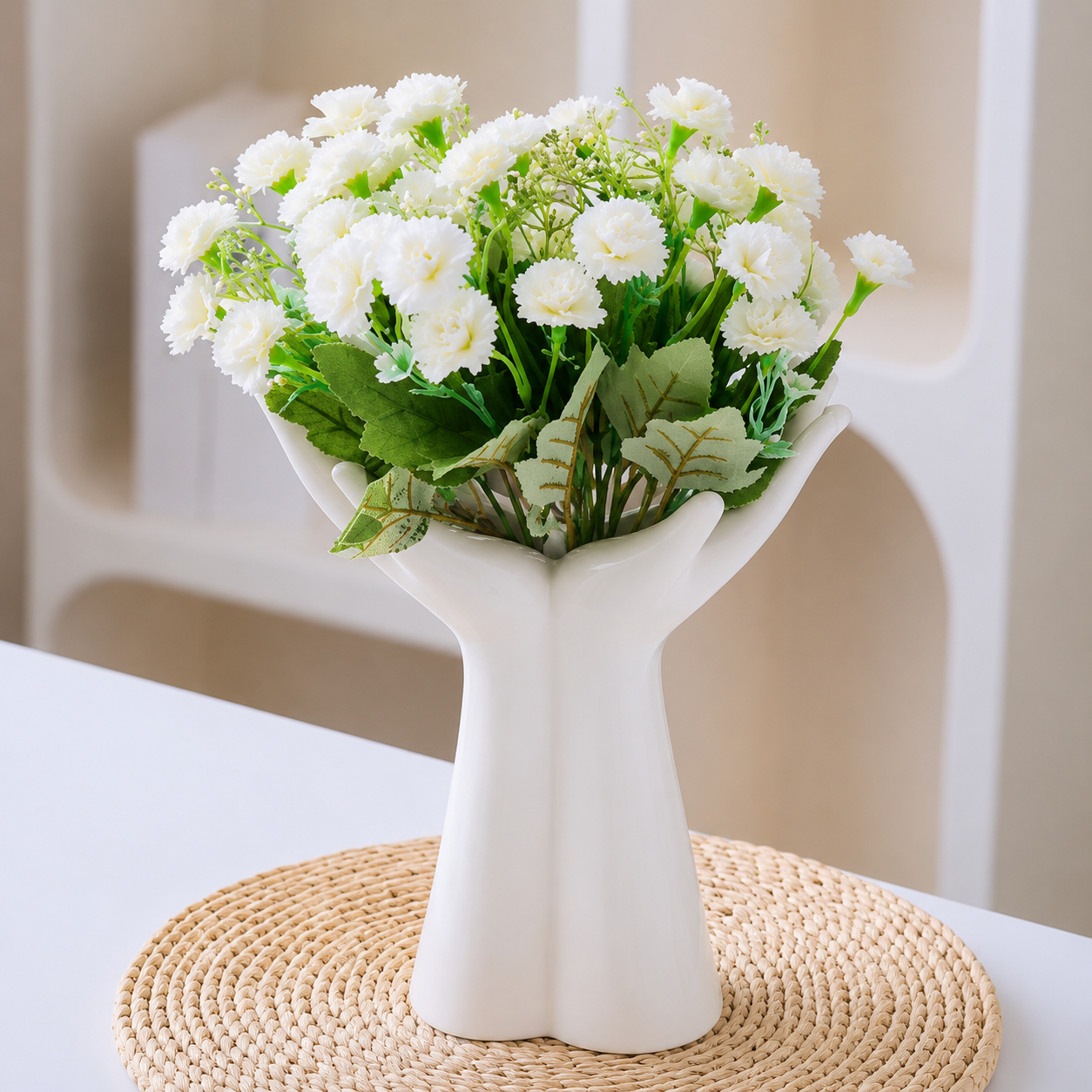 Sculptural white ceramic open palm vase styled with white flowers on a woven mat