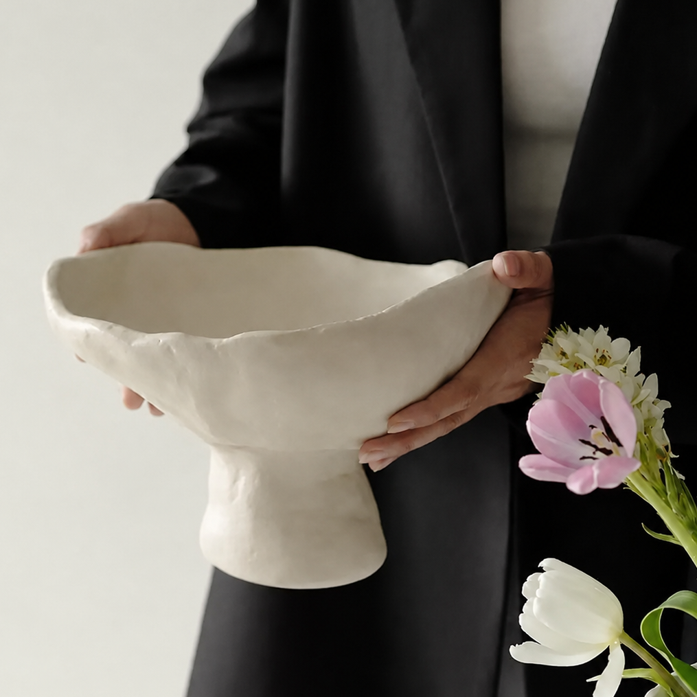 White ceramic pedestal bowl held by person showing sculptural organic shape