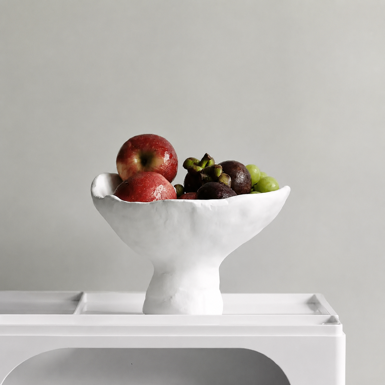 White ceramic pedestal fruit bowl styled with mixed fruit on modern console