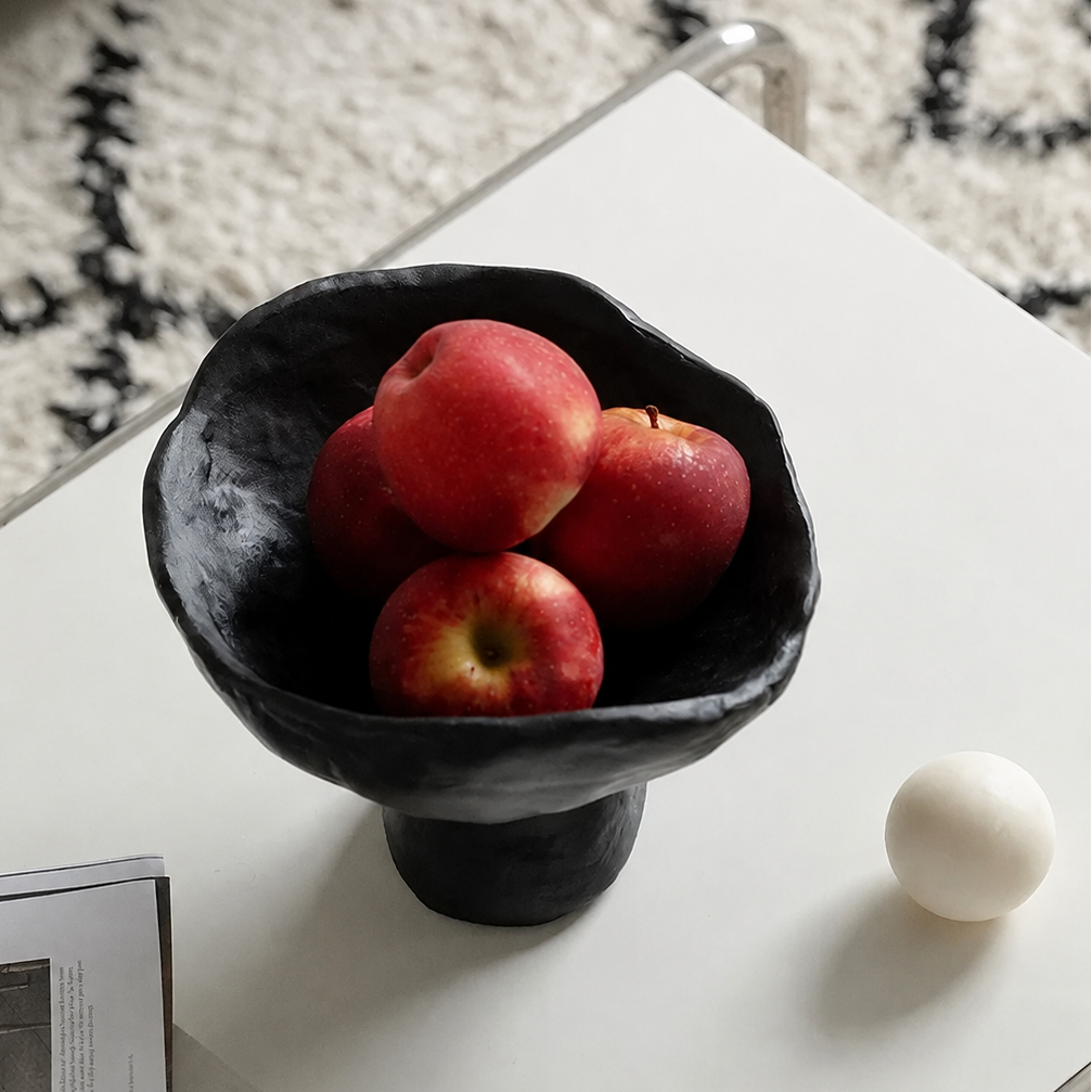 Black sculptural ceramic pedestal fruit bowl with red apples on modern table