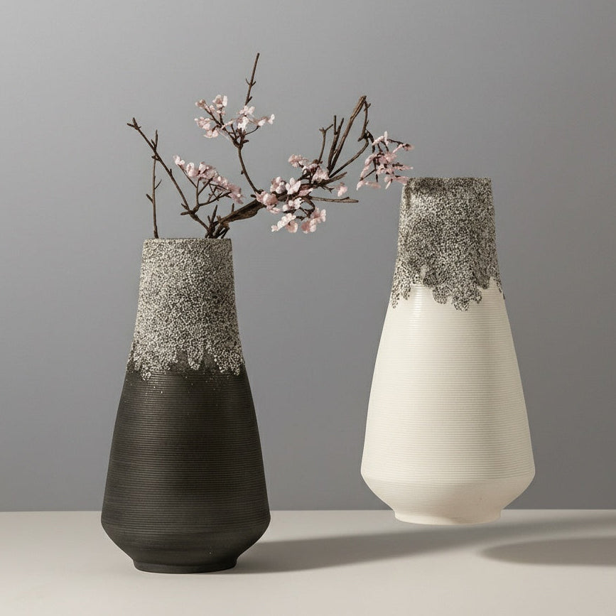 Black and white sculptural ceramic vases with flowering branches on neutral backdrop