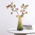 Amber green faceted glass vase styled with flowering branches on a modern side table