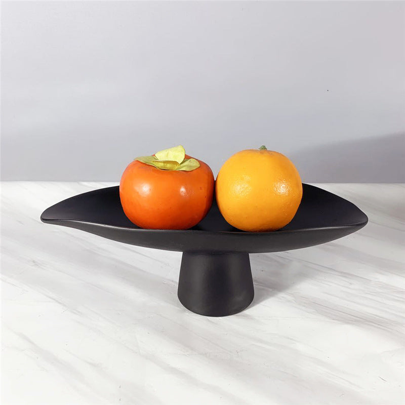Black sculptural resin pedestal bowl displaying oranges on a light marble surface