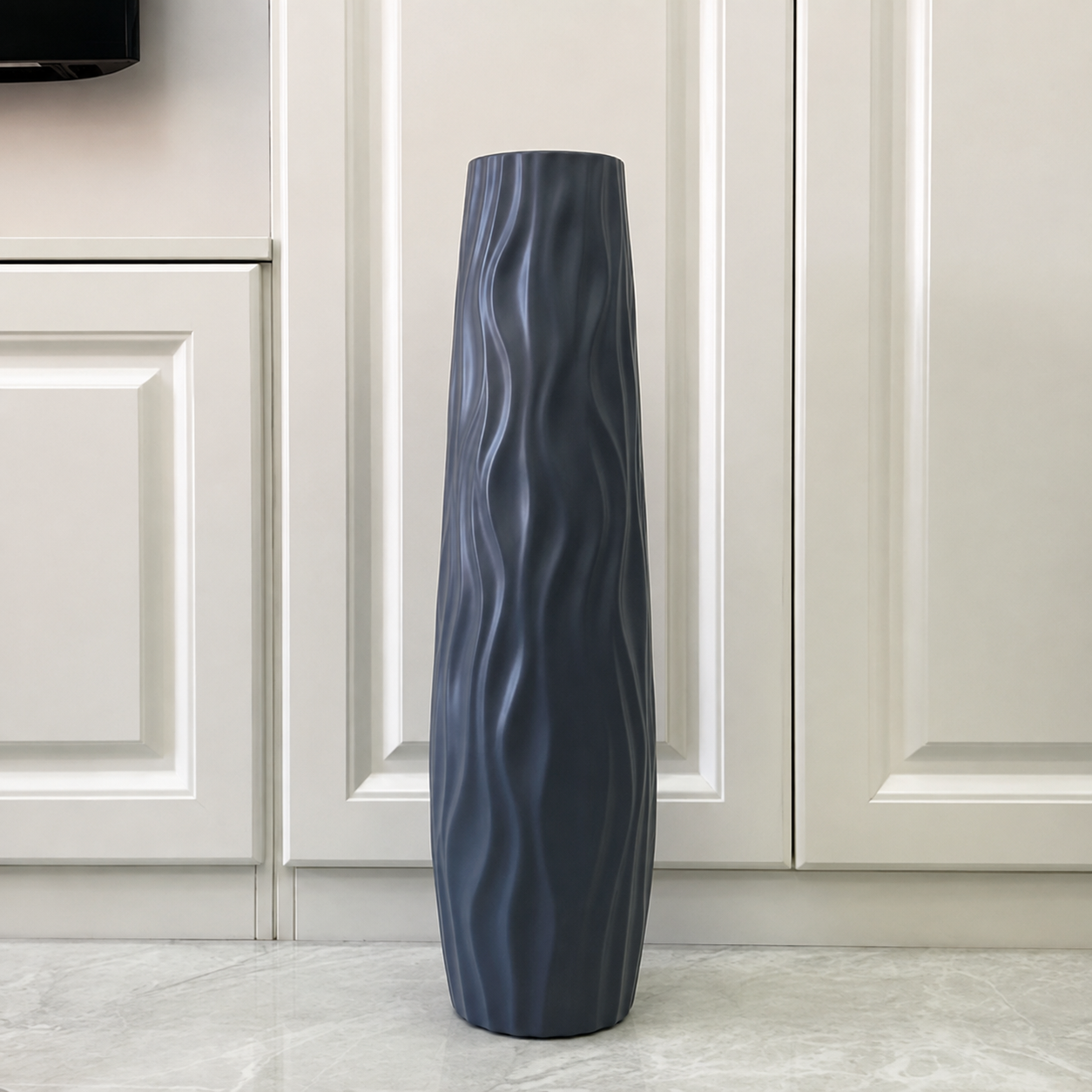 Gray wavy textured floor vase displayed against a modern paneled wall