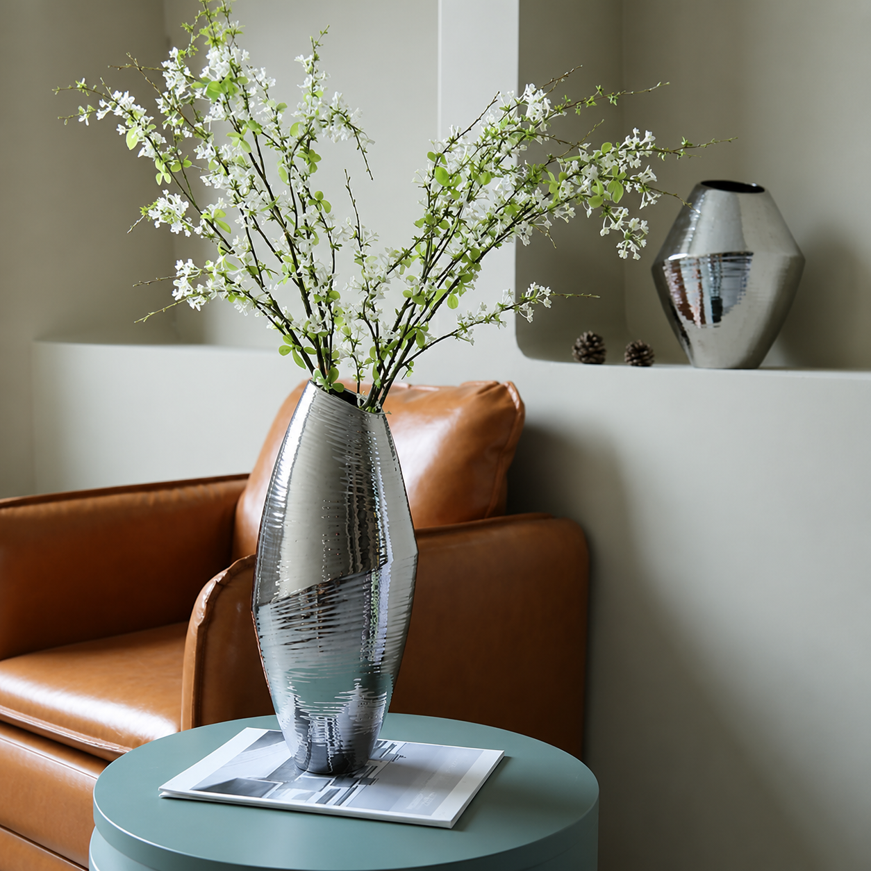 Tall silver ceramic vase with white blossoms on round side table