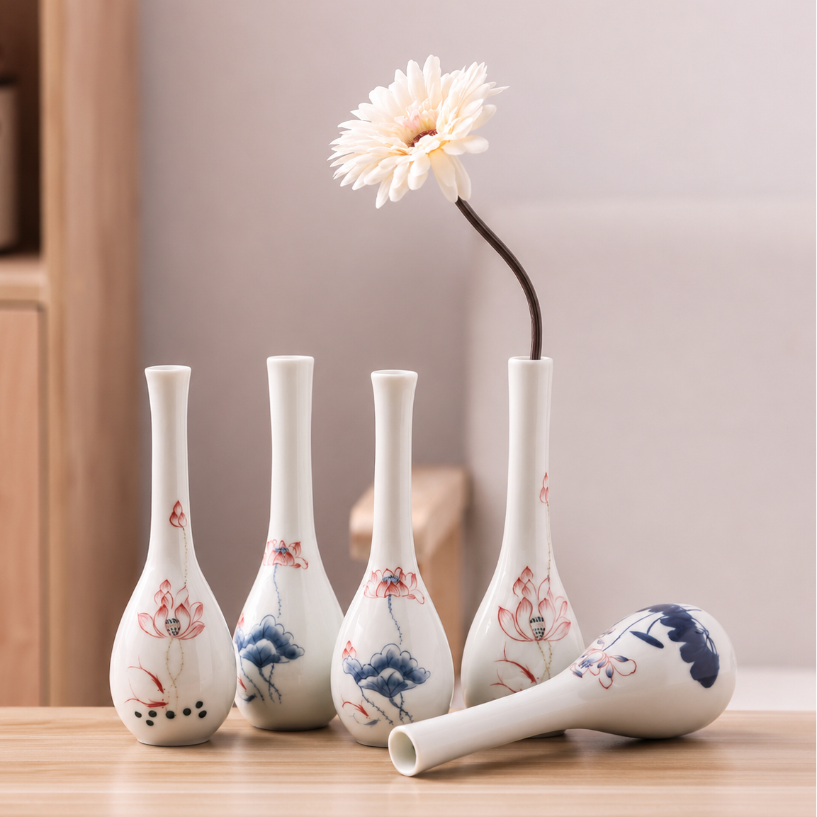 Assorted slim ceramic bud vases with lotus designs displayed together on a wooden table, including one vase with a single white flower