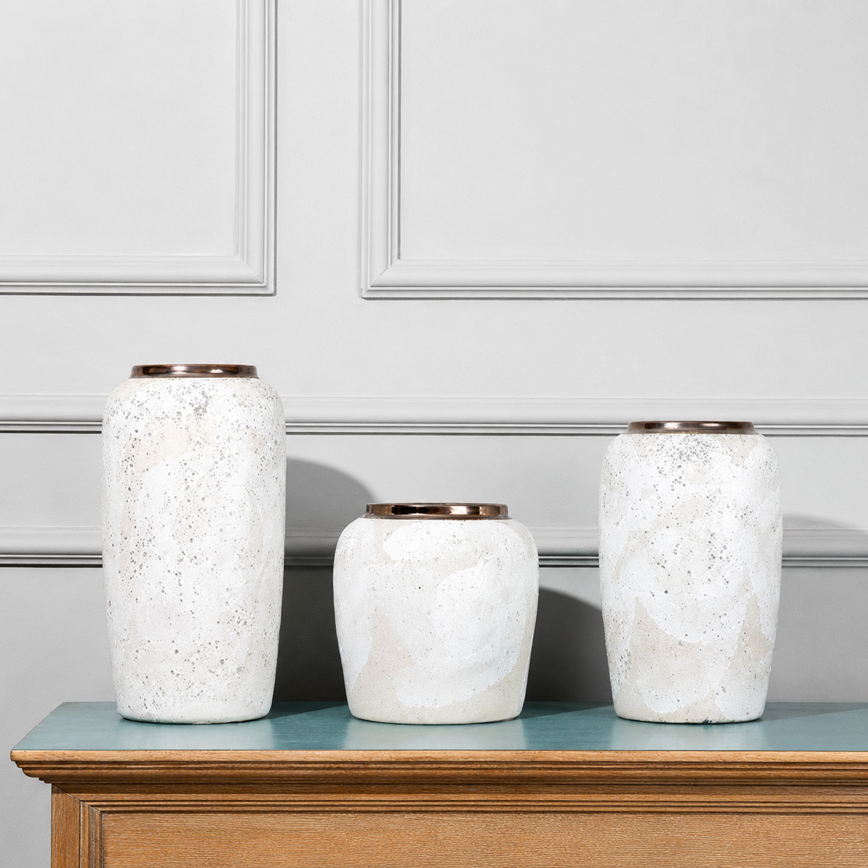 Set of speckled white ceramic vases with bronze rims displayed on a modern console table
