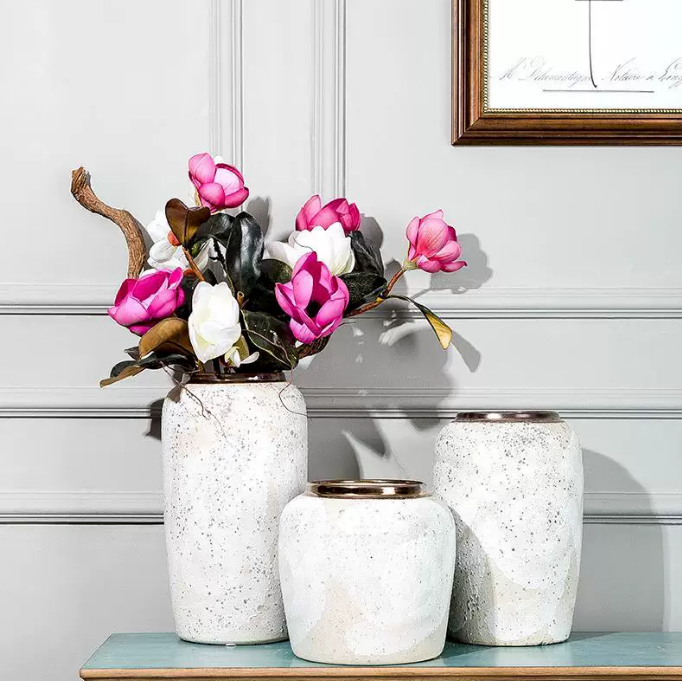 Speckled white ceramic vases with bronze rims styled with pink floral stems on a console table