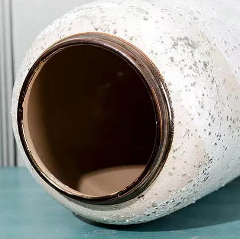 Close up of speckled white ceramic vase opening with dark bronze rim detail