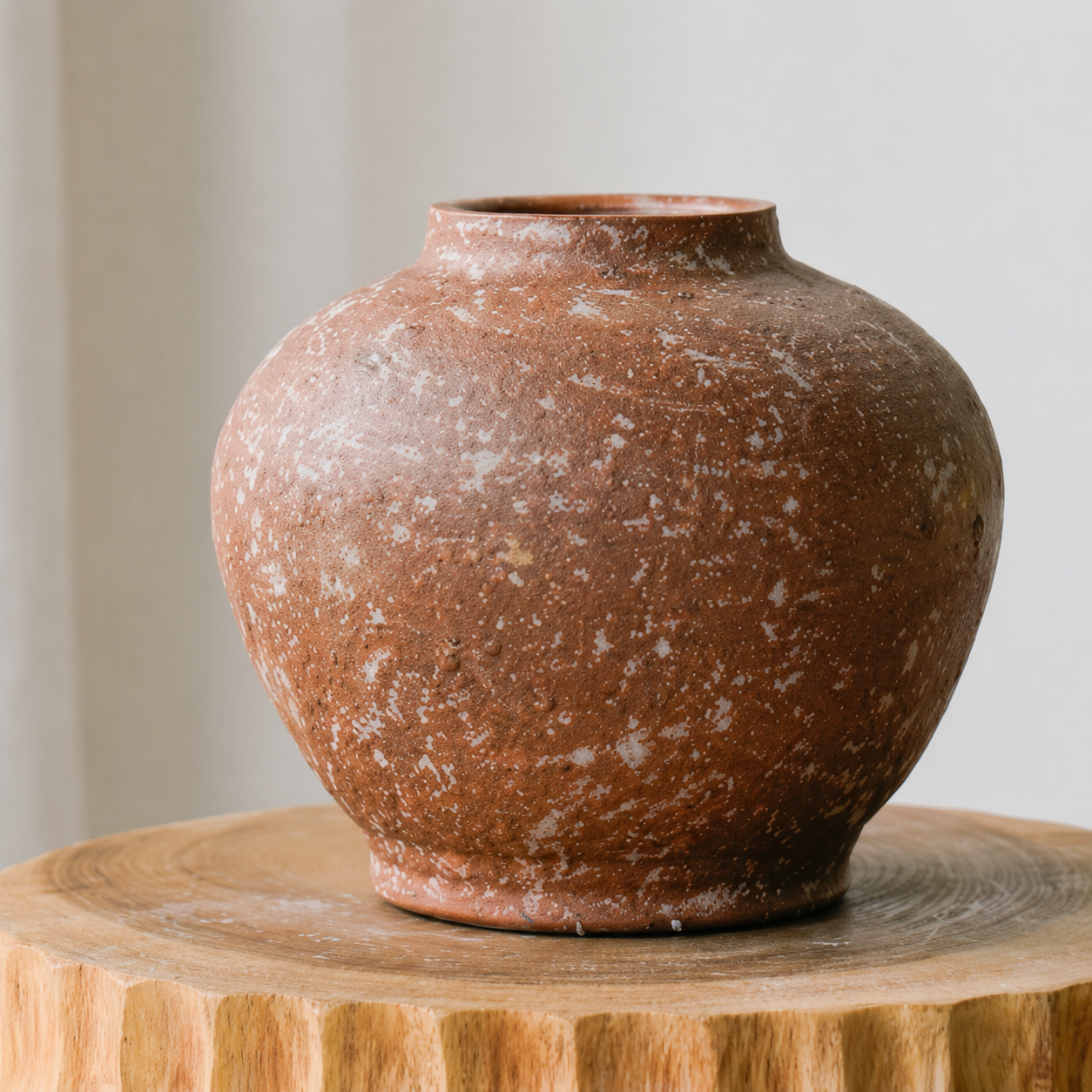 Round terracotta ceramic vase with speckled finish on wooden pedestal